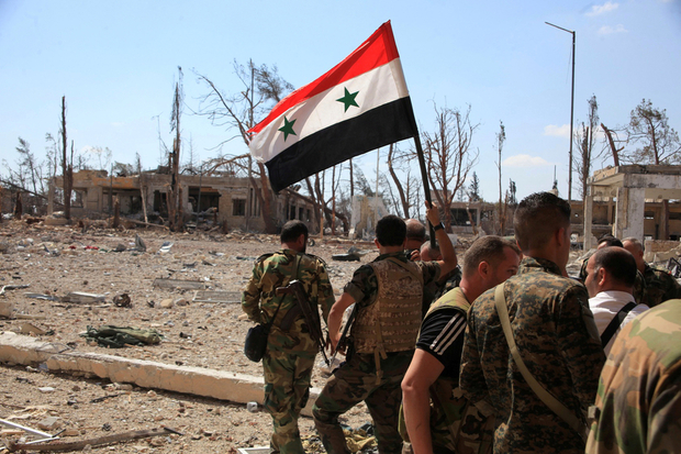 A file photo shows forces loyal to Syria's President Bashar al-Assad walking at a military complex as one of them holds up a Syrian national flag, after they recaptured areas in southwestern Aleppo on Sunday that rebels had seized last month