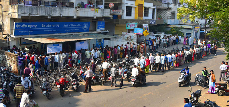 Bank customers waits next to a closed ATM as others queue to exchange old 500 and 1000 rupee notes and deposit money at a bank in Nagpur.India on November 11, 2016. Long queues formed outside banks in India as people crowded into deposit and withdraw money after the two largest denomination notes were taken out of circulation.